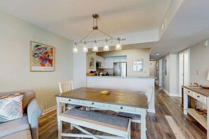 A dining area with a wooden table and bench, a hanging light fixture, and a kitchen in the background. - Caribbean Resort and Villas 1107 (Myrtle Beach)