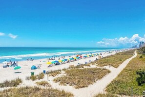 Een strand met heldere lucht, een zandstrand en een pad naar het water.