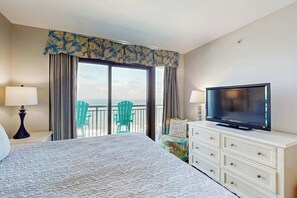 A hotel room with a large bed, a television, a dresser, and a balcony with chairs. - Caribbean Resort and Villas 1107 (Myrtle Beach)