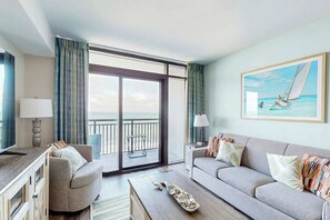 Een hotelkamer met balkon, een bank, een bijzettafeltje en een schilderij van een zeilboot.