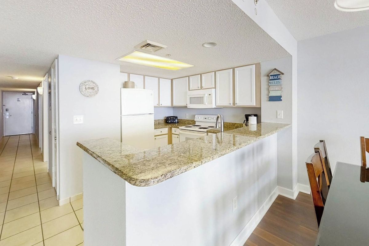 A modern kitchen with white cabinets, a granite countertop, and a built-in microwave.