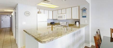 A modern kitchen with white cabinets, a granite countertop, and a built-in microwave.