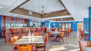 Ein geräumiges Restaurant mit mehreren Tischen, Stühlen, einer Bar und einem Deckenventilator.