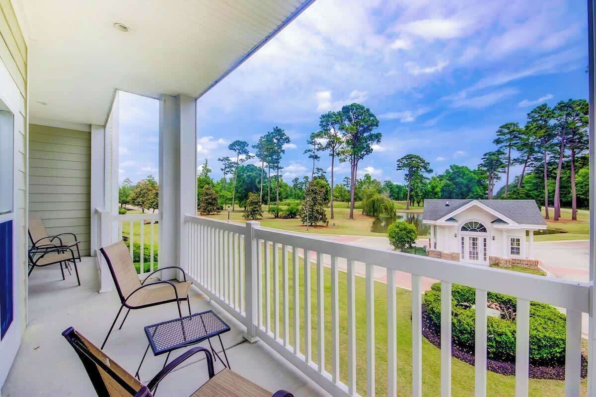 A covered porch with outdoor seating and a view of a residential area with trees and a house.