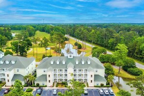A hotel with a central courtyard, multiple parking spaces, and a view of a lake and forested area. - *1001 World Tour 206 (Myrtle Beach)