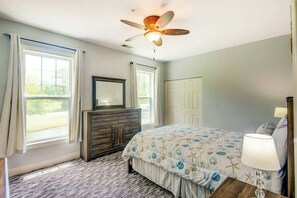 Ein Schlafzimmer mit Bett, Kommode, Deckenventilator und einem Fenster mit Vorhängen.
