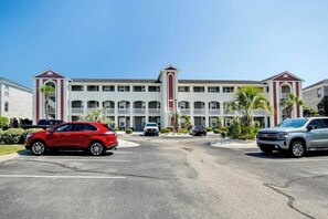 A multi-story hotel with a central courtyard, parking spaces, and a clear sky. - Plantation Harbour G-16 (Little River)