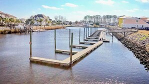 A waterfront property with a dock extending into a body of water, surrounded by residential buildings and vegetation. - Plantation Harbour G-16 (Little River)