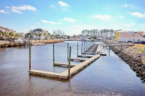 A waterfront property with a dock extending into a body of water, surrounded by residential buildings and vegetation. - Plantation Harbour G-16 (Little River)