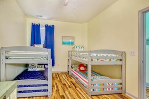 A room with bunk beds, a window with blue curtains, a small painting on the wall, and a door on the right. - Plantation Harbour G-16 (Little River)