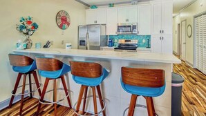 A modern kitchen with a bar area, stainless steel appliances, and a decorative clock. - Plantation Harbour G-16 (Little River)
