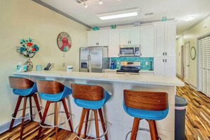 A modern kitchen with a bar area, stainless steel appliances, and a decorative clock. - Plantation Harbour G-16 (Little River)