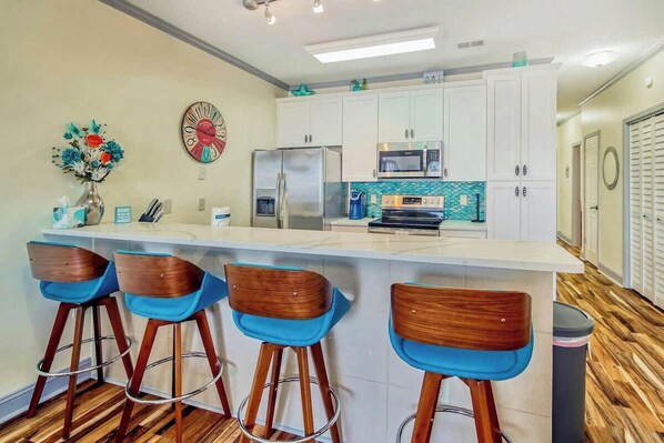 A modern kitchen with a bar area, stainless steel appliances, and a decorative clock. - Plantation Harbour G-16 (Little River)