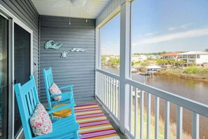A balcony with a view of a river and buildings, featuring a striped rug and blue chairs. - Plantation Harbour G-16 (Little River)