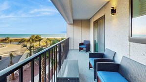 A balcony with a view of the beach, a seating area with chairs and a table, and a wall-mounted light fixture. - Renaissance Tower 211 (Myrtle Beach)
