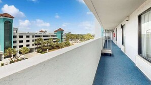 A hotel corridor with a blue carpet, a metal cart, and a view of a building with a red roof. - Caribbean Resort 525 (Myrtle Beach)