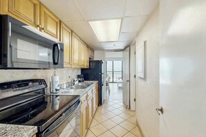 A kitchen with wooden cabinets, stainless steel appliances, and a tiled floor. - Caribbean Resort 525 (Myrtle Beach)
