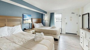 A hotel room with two beds, a nightstand, a lamp, a dresser, and a door leading to a balcony. - Caribbean Resort 525 (Myrtle Beach)