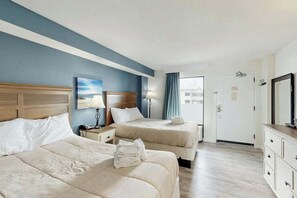 Ein Hotelzimmer mit zwei Betten, einem Nachttisch, einer Lampe, einem Schminktisch und einer Tür, die auf einen Balkon führt.