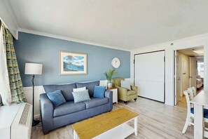 A modern living room with a grey sofa, a wooden coffee table, a floor lamp, a clock, and a painting on the wall. - Caribbean Resort 525 (Myrtle Beach)