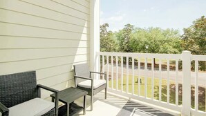 A covered porch with a white railing, a wicker chair, and a small table. - 1017 World Tour Unit 204 (Myrtle Beach)