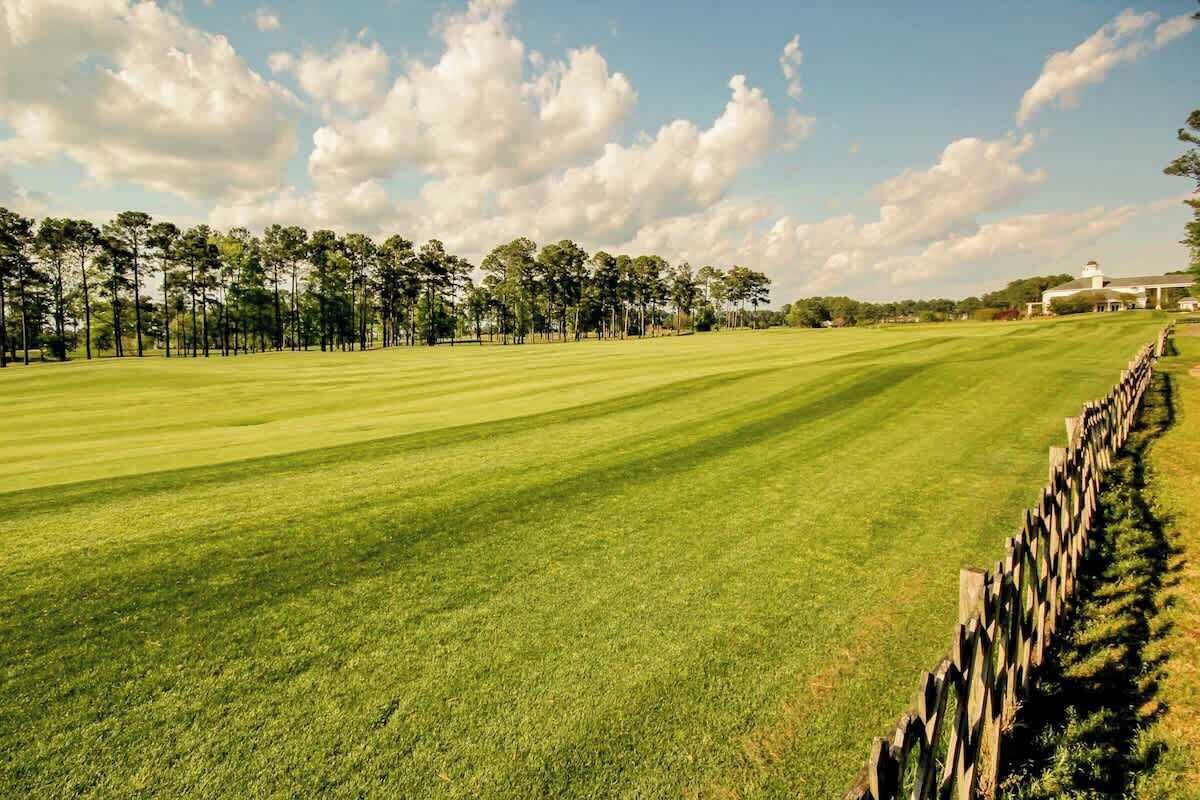 Ein Golfplatz mit Holzzaun und Bäumen im Hintergrund.