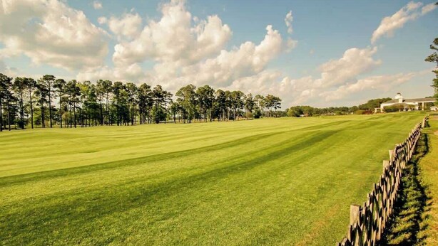 A golf course with a wooden fence and trees in the background. - 1017 World Tour Unit 204 (Myrtle Beach)