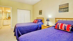 A bedroom with two beds, a nightstand with a lamp, a wardrobe, and a painting on the wall. - 1017 World Tour Unit 204 (Myrtle Beach)