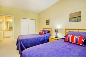 A bedroom with two beds, a nightstand with a lamp, a wardrobe, and a painting on the wall. - 1017 World Tour Unit 204 (Myrtle Beach)