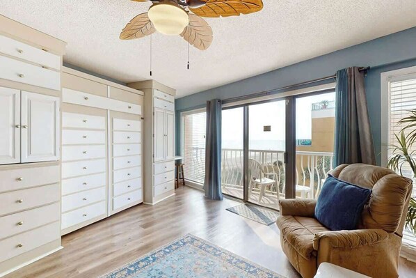 A spacious room with a ceiling fan, a large sliding glass door to a balcony, and a brown leather chair with a cushion. - St Clement's Unit 409 (Myrtle Beach)