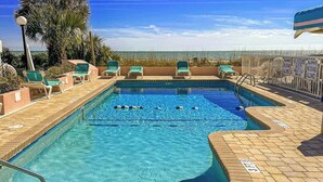 A swimming pool with clear blue water, surrounded by lounge chairs and a view of the ocean. - St Clement's Unit 409 (Myrtle Beach)