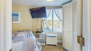 A bedroom with a bed, a desk, a television, a window with curtains, and a wardrobe. - St Clement's Unit 409 (Myrtle Beach)