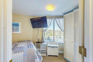 Quarto com cama, escrivaninha, televisão, janela com cortinas e guarda-roupa.