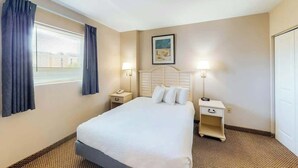 Una habitación de hotel con una cama, dos mesitas de noche, un ventanal con cortinas y un cuadro colgado en la pared.