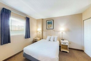 A hotel room with a bed, two bedside tables, a nightstand, a window with curtains, and a wall-mounted picture. - Harbourgate Unit 132 (North Myrtle Beach)