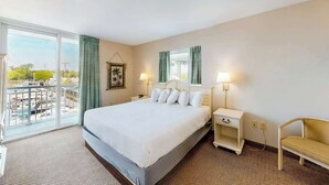 Habitación de hotel con una cama grande, una silla, una mesita de noche y una ventana con vistas al exterior.