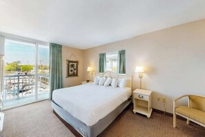 A hotel room with a large bed, a chair, a nightstand, and a window with a view of the outside. - Harbourgate Unit 132 (North Myrtle Beach)
