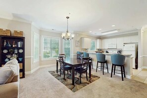 A dining area with a table and chairs, a kitchen with white cabinets, and a chandelier. - Luster Leaf Unit 105 (Myrtle Beach)