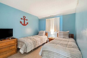 Quarto com duas camas, televisão e cómoda de madeira.