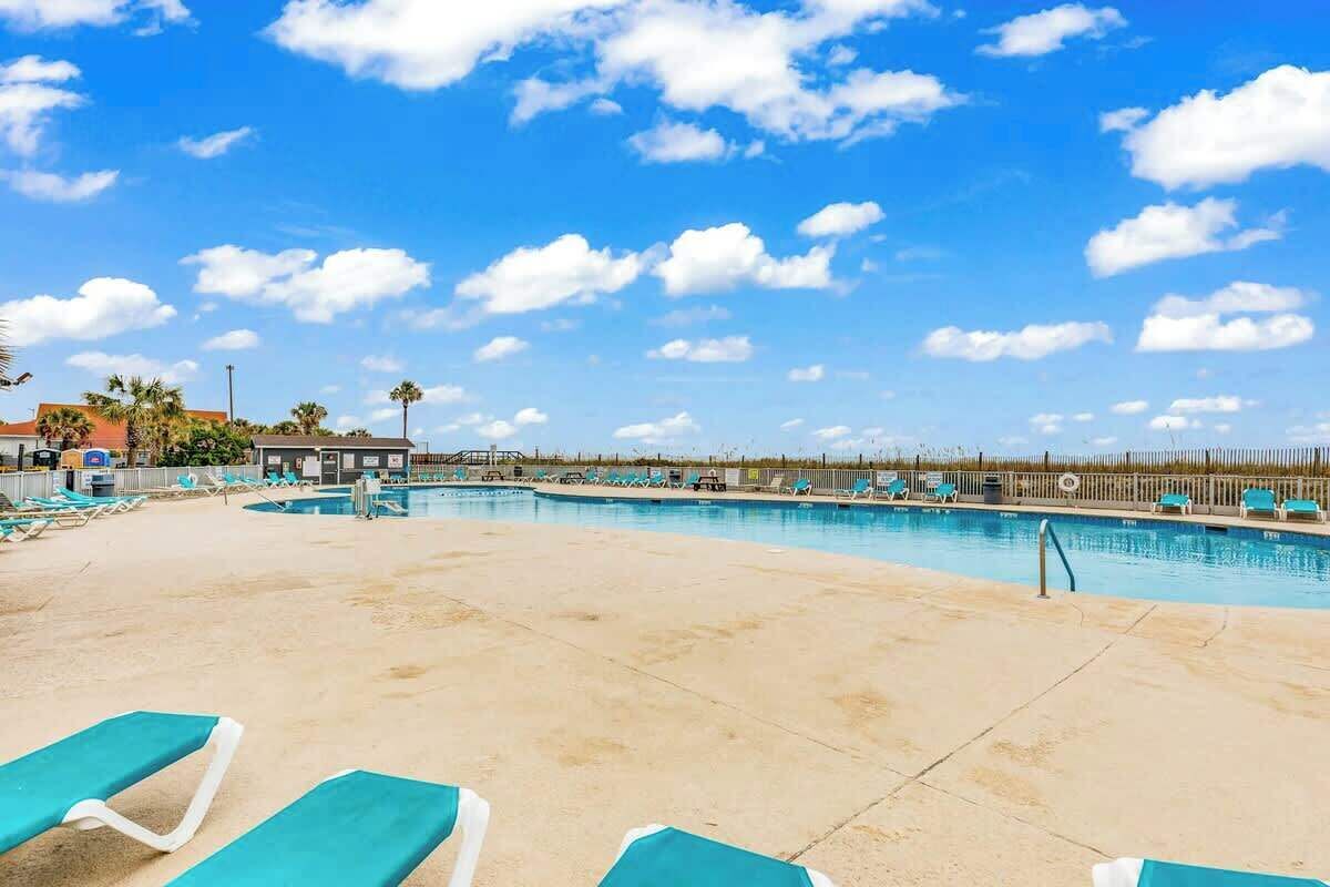 A pool area with lounge chairs and a clear sky.