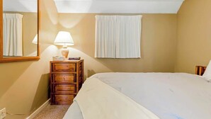 A bedroom with a bed, a nightstand, a lamp, a mirror, and a window with curtains. - Myrtle Beach Resort B-229 (Myrtle Beach)