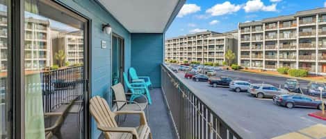 A balcony with chairs and a table, overlooking a parking lot and buildings.