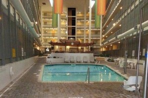 Interior de hotel com área de piscina central, vários andares com varandas e um espaço de estar coberto.