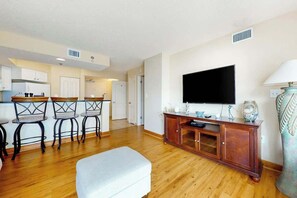 Ein Wohnzimmer mit Flachbildfernseher, Holzschrank und weißem Hocker.