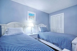 Ein Schlafzimmer mit zwei Betten, weißen Kopfteilen und einer blau-weißen Bettdecke.
