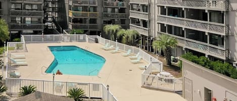 Un hotel de varios pisos con una piscina central rodeada de sillones de descanso y un área cercada.