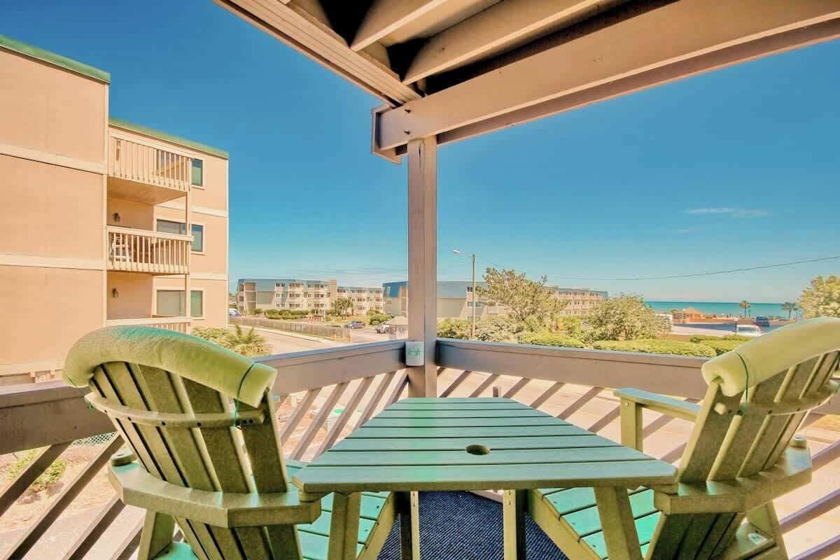 A balcony with two chairs and a table, overlooking a residential area and a body of water.