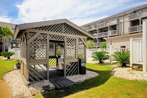 Ein Pavillon mit Gitterdach, umgeben von einem Kiesweg und kleinen Pflanzen.