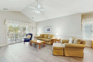 Ein geräumiges Wohnzimmer mit hoher Decke, Deckenventilator, einer Sofagarnitur, einem Couchtisch und einem Essbereich mit Tisch und Stühlen.