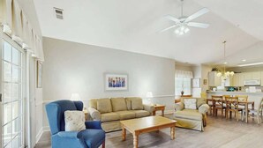 A spacious living room with a sofa, armchair, and coffee table, a dining area with chairs, and a kitchen in the background. - Magnolia Pointe Unit 305 (Myrtle Beach)